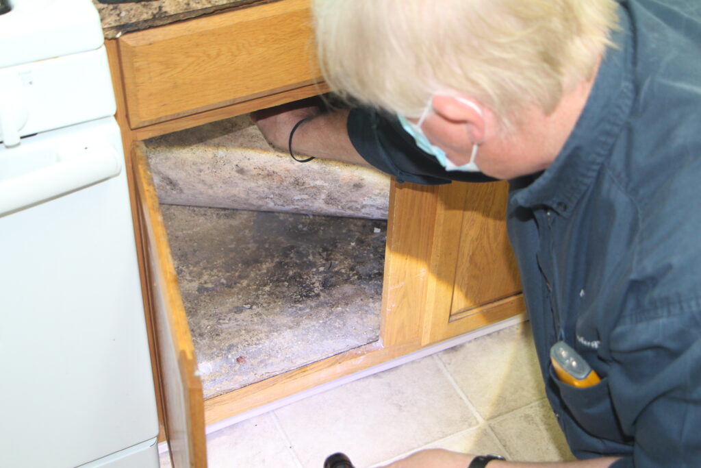 An INX Indoor Air Quality mold inspector inspecting for mold in under a kitchen sink.